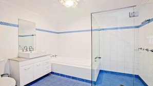 Un baño con lavamanos blanco, espejo y retrete, bañera y zona de ducha con paredes y suelo de azulejos azules.