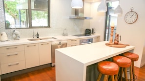 A modern kitchen with a central island, bar stools, a coffee machine, and a clock on the wall. - CHAPTER 11 DELANY: Bright (Bright)