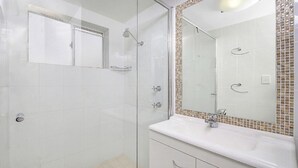 Uma casa de banho moderna com cabine de duche em vidro, lavatório branco com espelho e chão em mosaico.