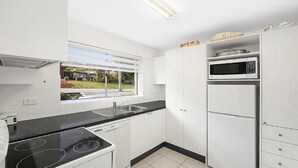Cozinha moderna com armários brancos, bancada preta, micro-ondas embutido e janela com vista para uma casa e gramado.