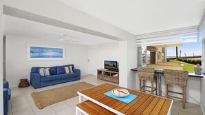 Uma sala de estar moderna com um sofá azul, uma mesa de centro de madeira e um rack para TV.