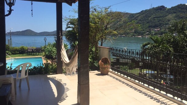 A covered outdoor area with a pool, chairs, and a hammock. - Beautiful beachfront house with pool and barbecue area (mangaratiba)