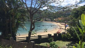 A coastal view with a beach, palm trees, and a stone wall. - Beautiful beachfront house with pool and barbecue area (mangaratiba)