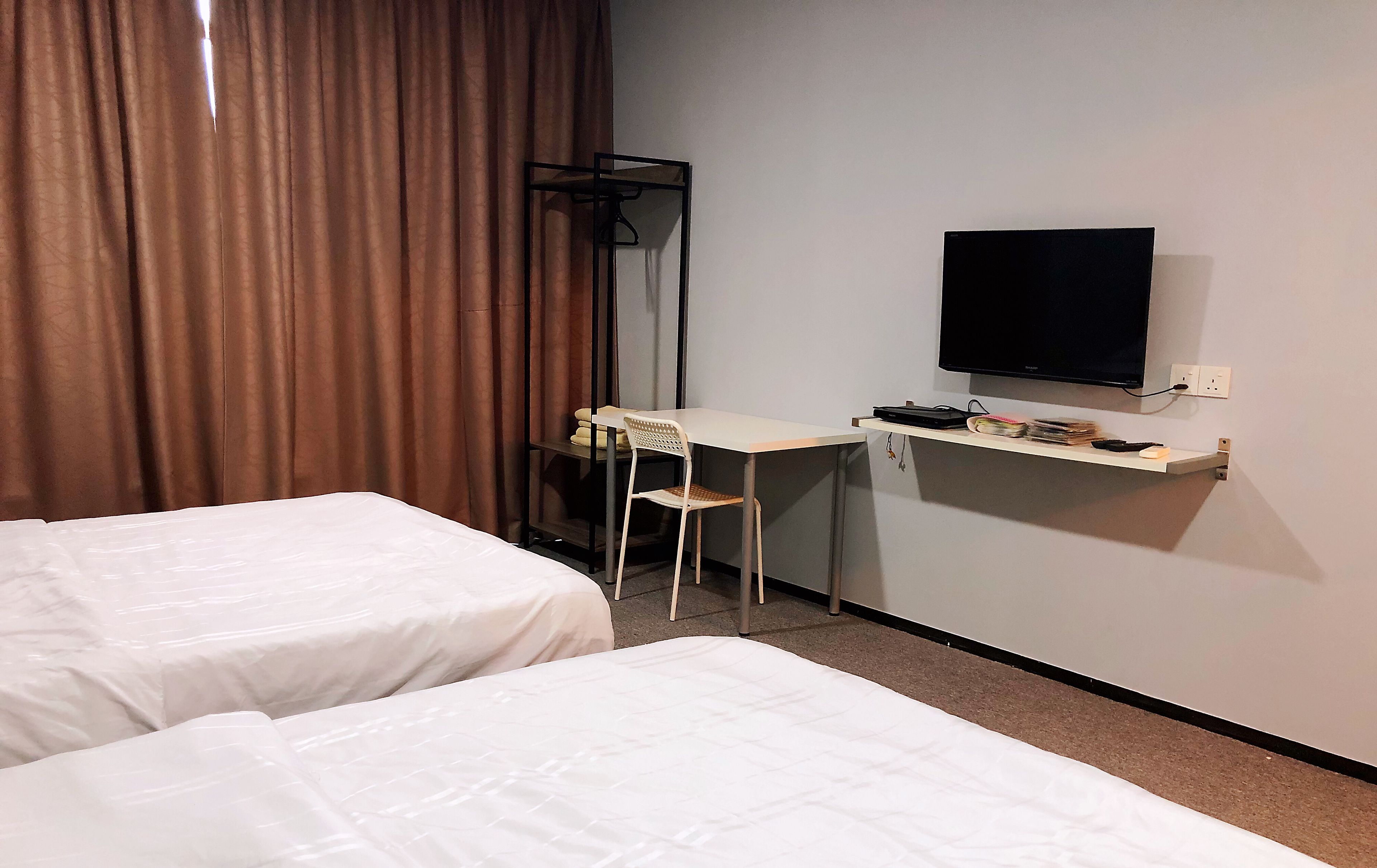 Une chambre d’hôtel avec deux lits, un bureau avec une chaise, une télévision et une étagère avec divers objets.