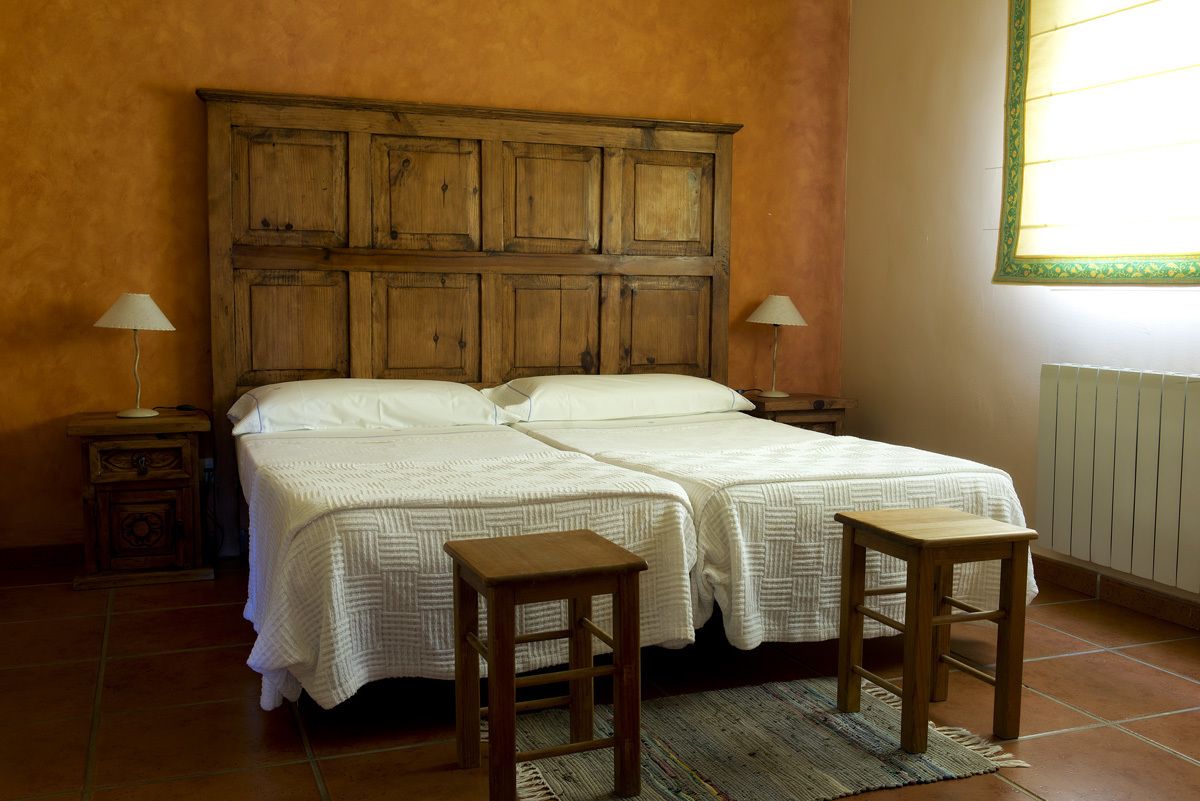 A double bed with two nightstands, each with a lamp, in a room with orange walls and a window with a green frame.