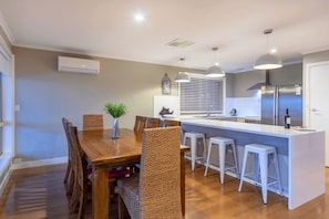 A modern kitchen with a central island, bar stools, and a dining area with a wooden table and wicker chairs.
