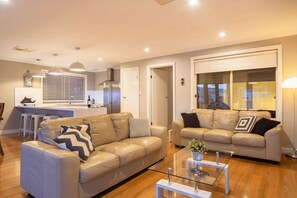 A modern living room with two leather sofas, a glass coffee table, and a kitchen area in the background.