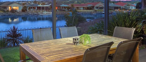 A covered outdoor dining area with a view of a lake and houses in the background.