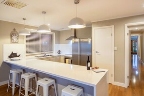 A modern kitchen with a central island, stainless steel appliances, pendant lighting, and a view into the adjacent living area.