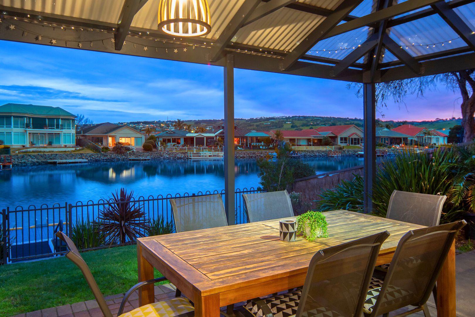 A covered outdoor dining area with a view of a lake and houses in the background.