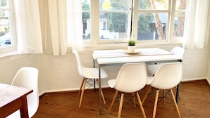 A dining area with a wooden table, white chairs, and a window with curtains. - Free parking & 3 min walk to beach! (Bondi Beach)