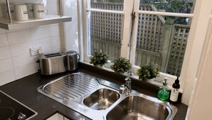 A modern kitchen with a stainless steel sink, a built-in oven, and a toaster. There are potted plants on the windowsill and a bottle of hand soap on the counter. - Free parking & 3 min walk to beach! (Bondi Beach)