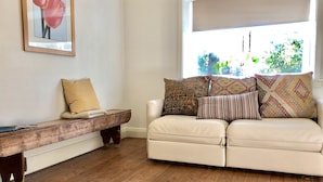 A cozy living room with a wooden bench, a white sofa with patterned cushions, and a framed picture on the wall. - Free parking & 3 min walk to beach! (Bondi Beach)