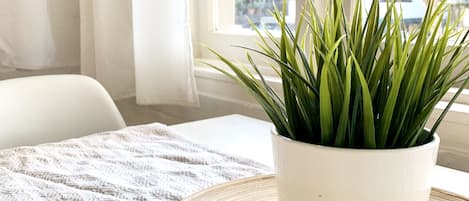 A potted plant on a round wooden tray on a patterned rug, near a window with sheer curtains.
