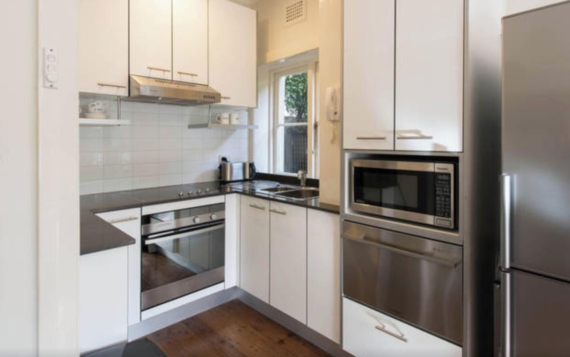 Een moderne keuken met witte kastjes, roestvrijstalen apparatuur en een houten vloer.