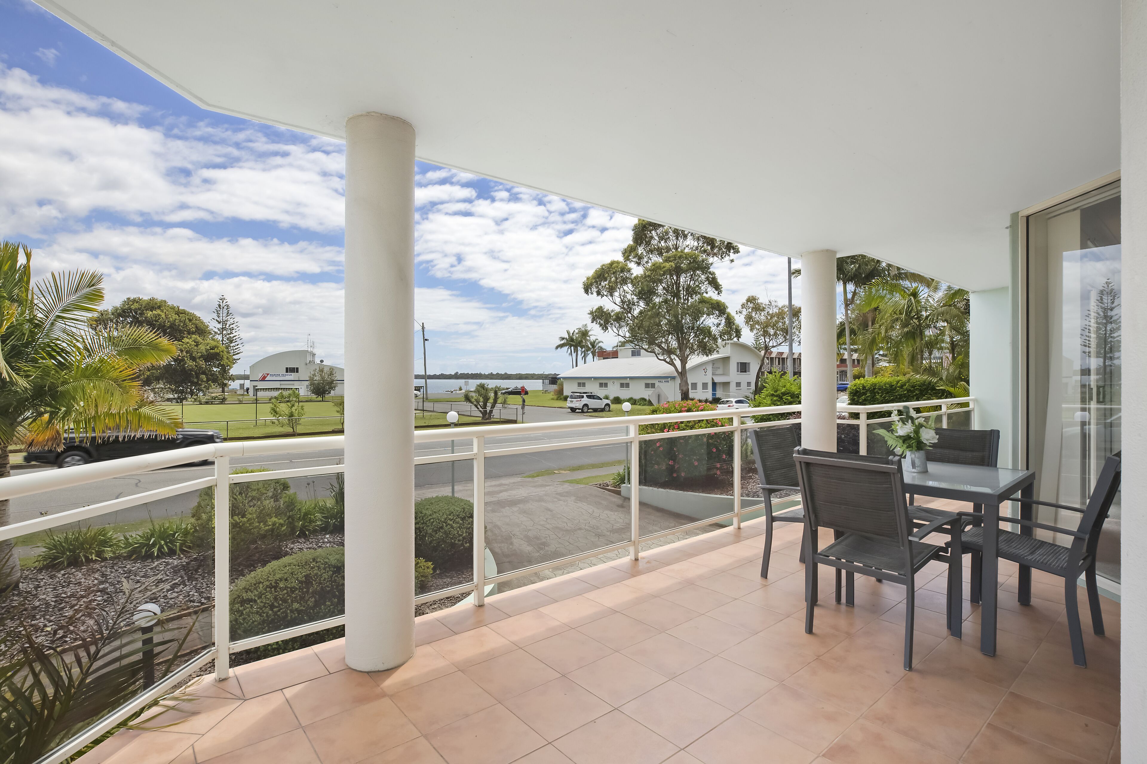 A covered outdoor area with a table and chairs, a view of the surrounding landscape, and a building with a sign.