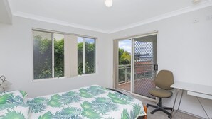 A bedroom with a bed, a desk, and a chair. There are two windows and a door leading to a balcony.