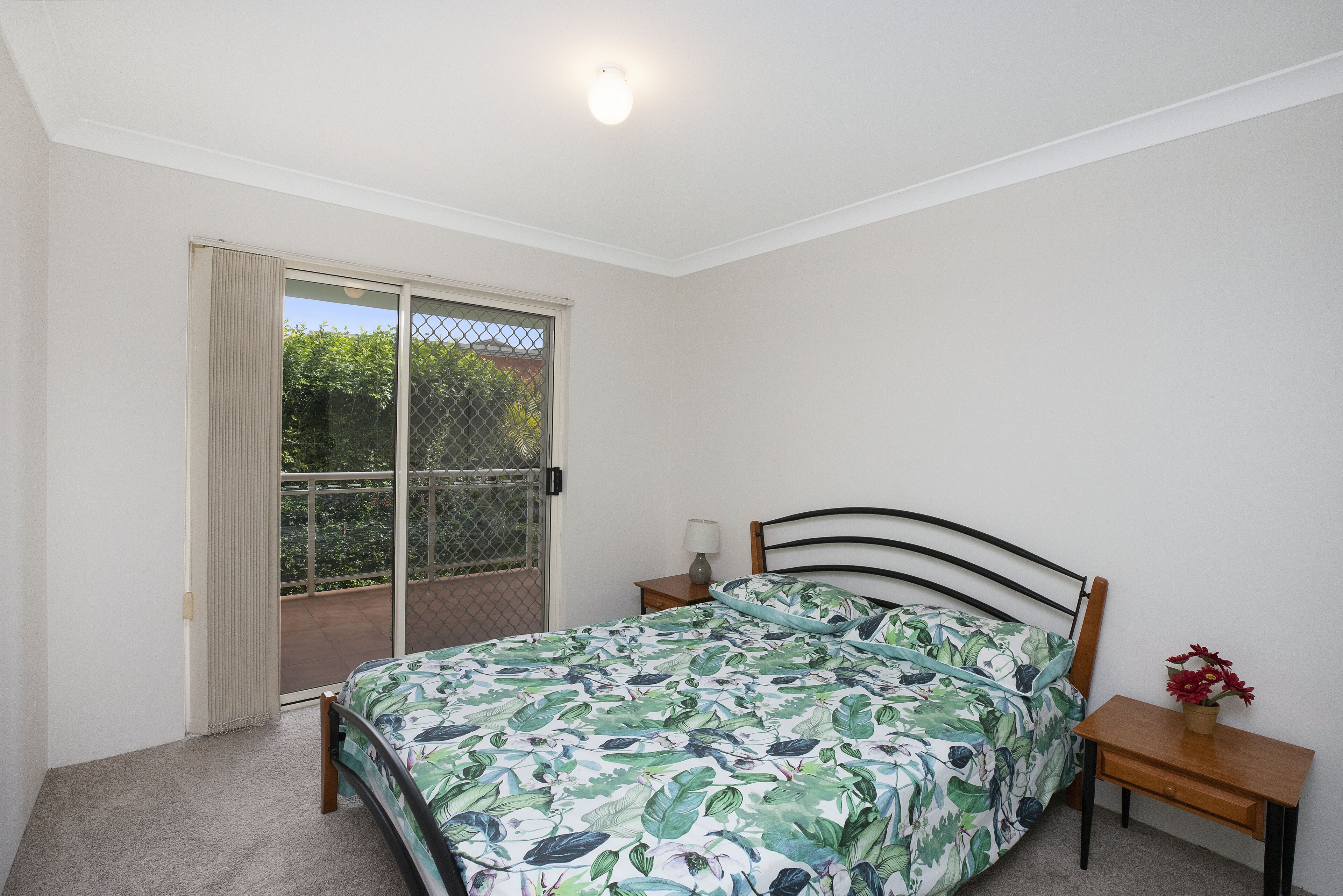 Une chambre à coucher comprenant un lit, une table de chevet, une lampe et une vue sur l’extérieur, accessible par une porte coulissante.
