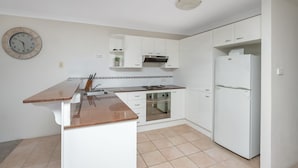 A kitchen with white cabinets, a stainless steel oven, a refrigerator, and a clock on the wall.