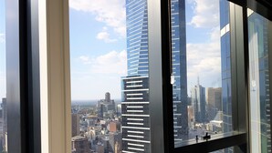 Une vue depuis une fenêtre d’un immeuble de grande hauteur, donnant sur un paysage urbain avec des gratte-ciel modernes et une rivière.