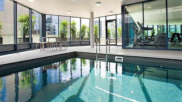 Une piscine intérieure moderne avec des parois en verre transparent, un toit ouvrant et du matériel d’exercice.