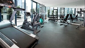 Une salle de sport moderne équipée de machines de cardio, d’appareils de musculation et de grandes fenêtres offrant une vue sur la ville.