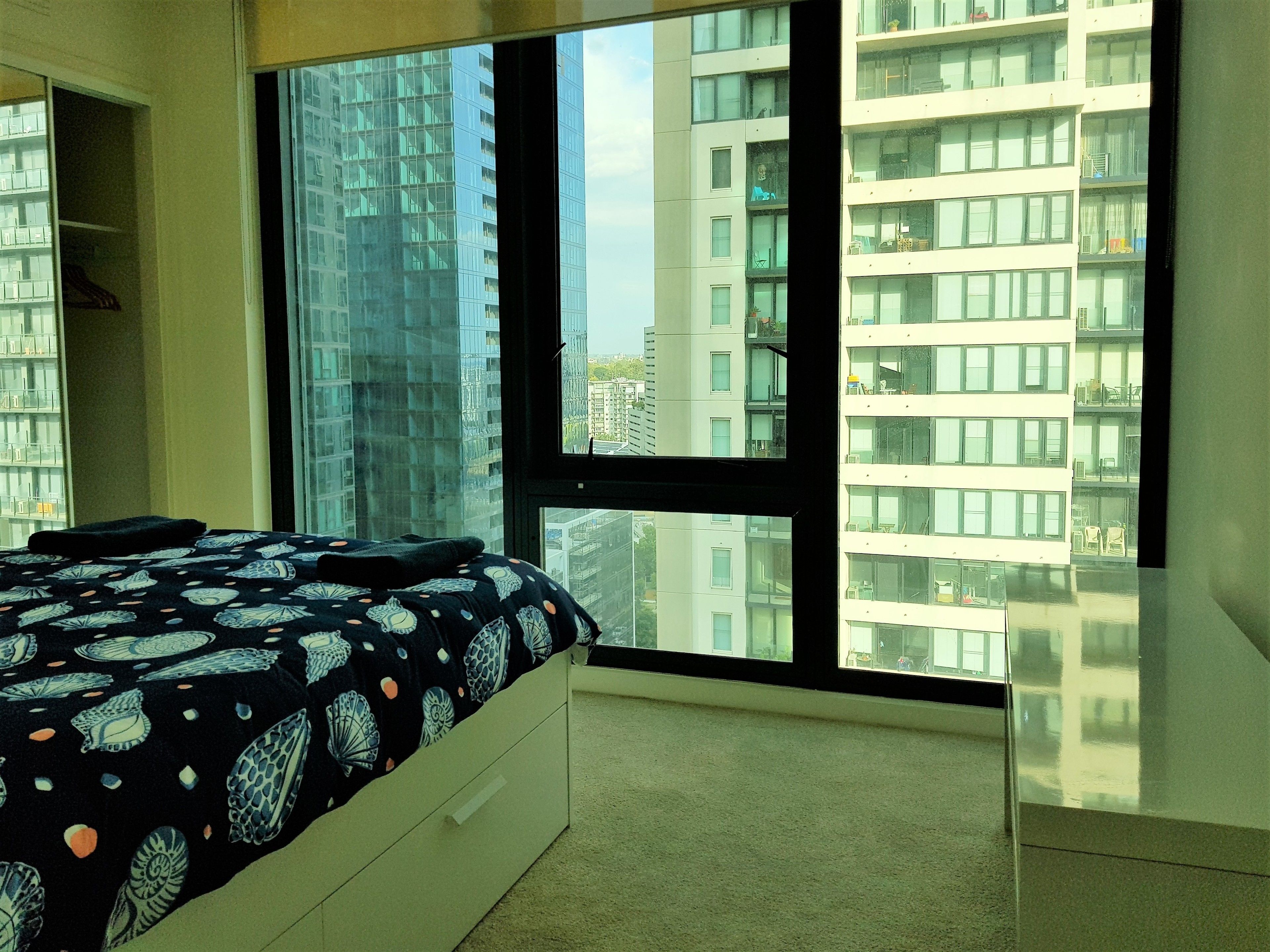 A bedroom with a large window, a bed with a patterned bedspread, and a white dresser.