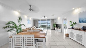 A spacious living area with a large dining table, comfortable seating, a TV, and a balcony with a scenic view. - Lagoon 206 Hamilton Island by HamoRent (Hamilton Island)
