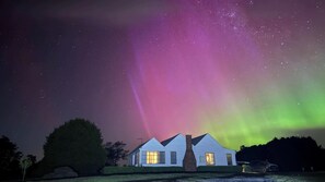 Une maison avec deux fenêtres apparentes, une cheminée et une voiture garée devant.