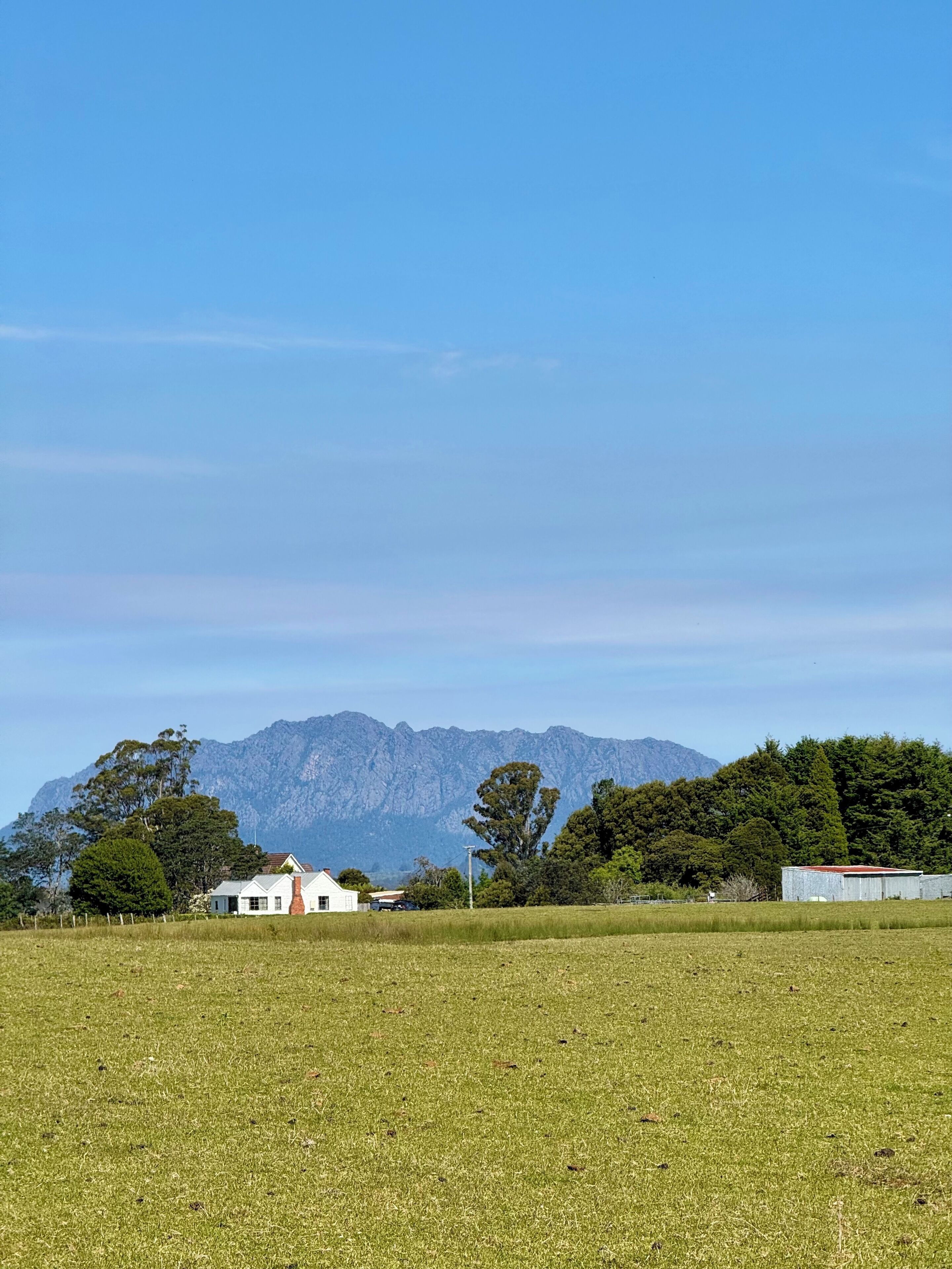 Landelijk landschap met een veld, een wit huis en een bergketen op de achtergrond.