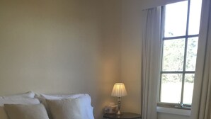 A neatly made bed with a white duvet and pillows, a bedside lamp, and a window with curtains. - Buttons Cottage underneath the Milky Way (Nietta)