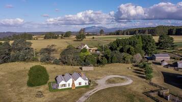 An aerial view of a rural property with a white house, barns, and a fenced area.