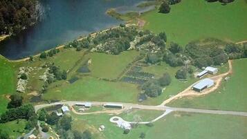 An aerial view of a property with a lake, green fields, and several buildings including a large white structure.