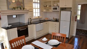 A compact kitchen with white cabinets, a black countertop, and a dining area with a wooden table and chairs. - Buttons Cottage underneath the Milky Way (Nietta)