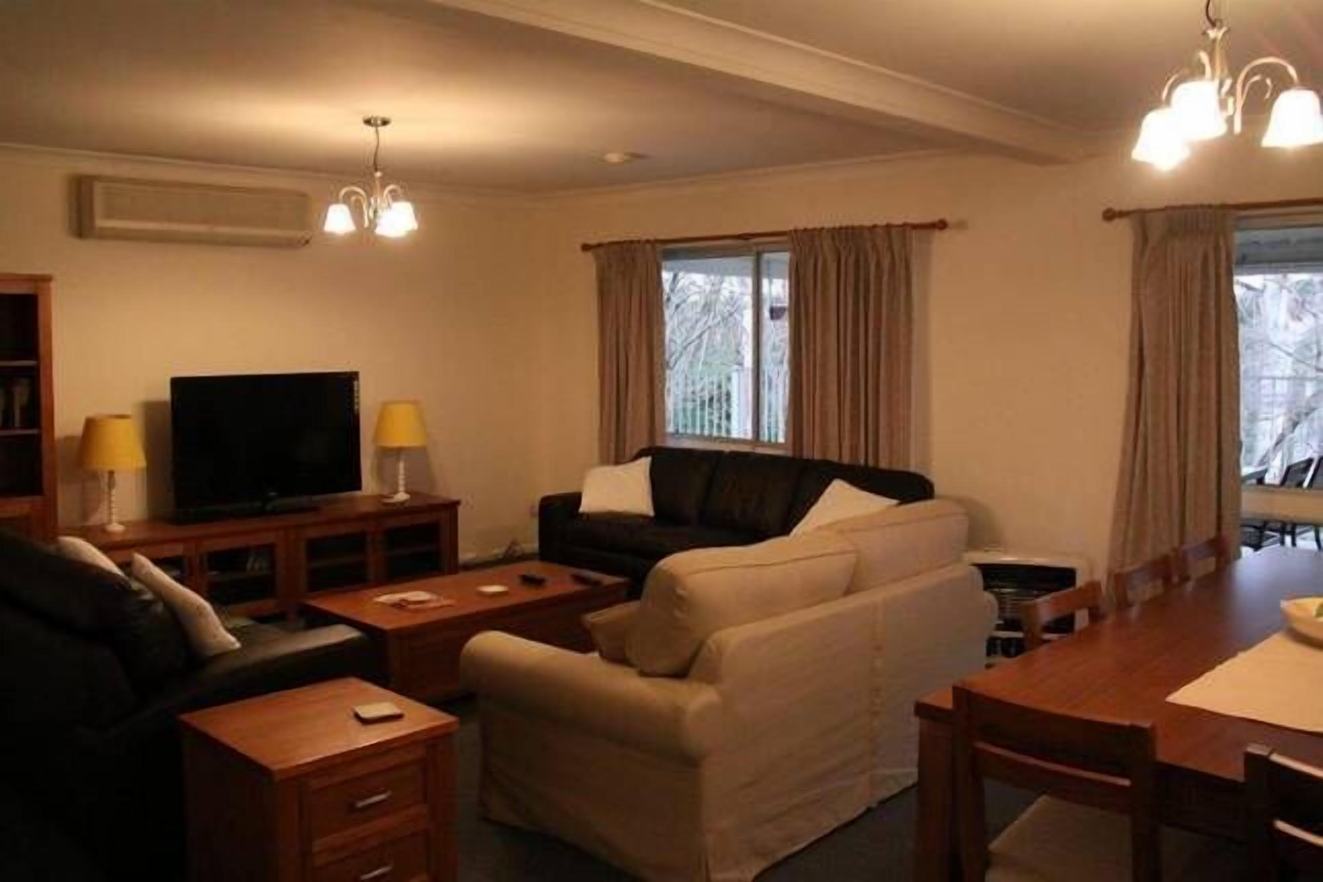 Ein Wohnzimmer mit Fernseher, Sofas, einem Esstisch und einer Deckenleuchte.