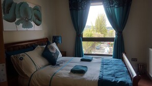 Ein Schlafzimmer mit Bett, Kissen, einer Lampe und Blick auf eine Straße durch ein Fenster.