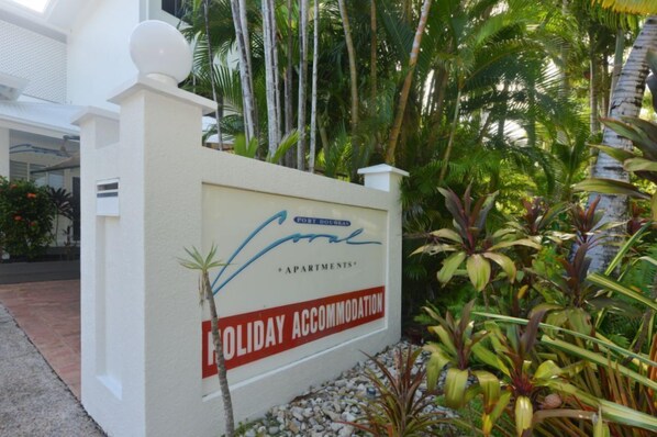 En skylt för Port Douglas Apartments med en tropisk trädgård i bakgrunden.