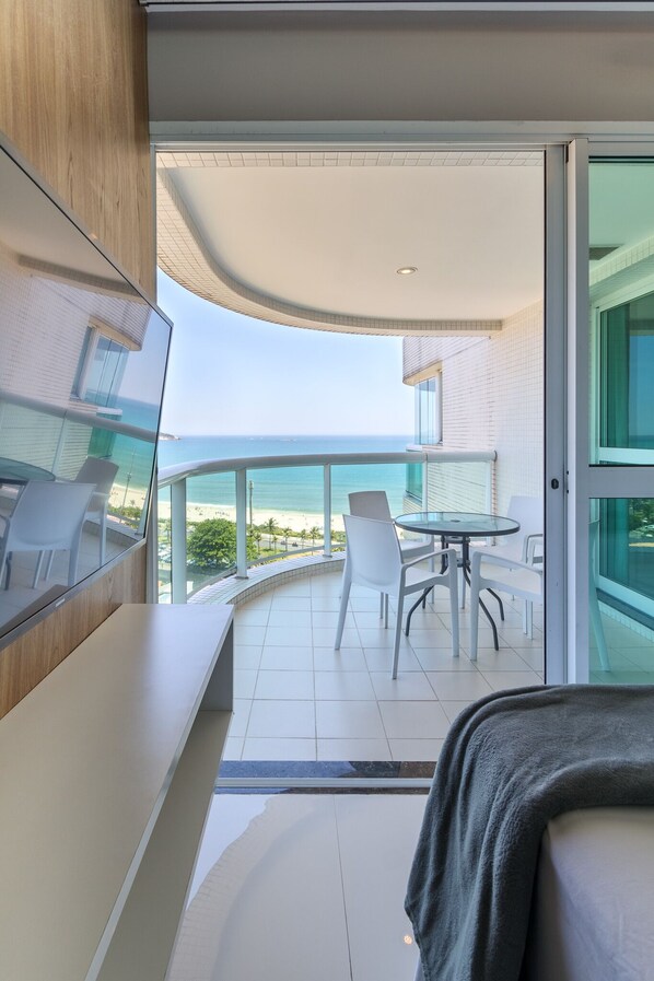 A modern balcony with a view of the ocean, a glass door leading to the interior, and a small dining area with chairs.