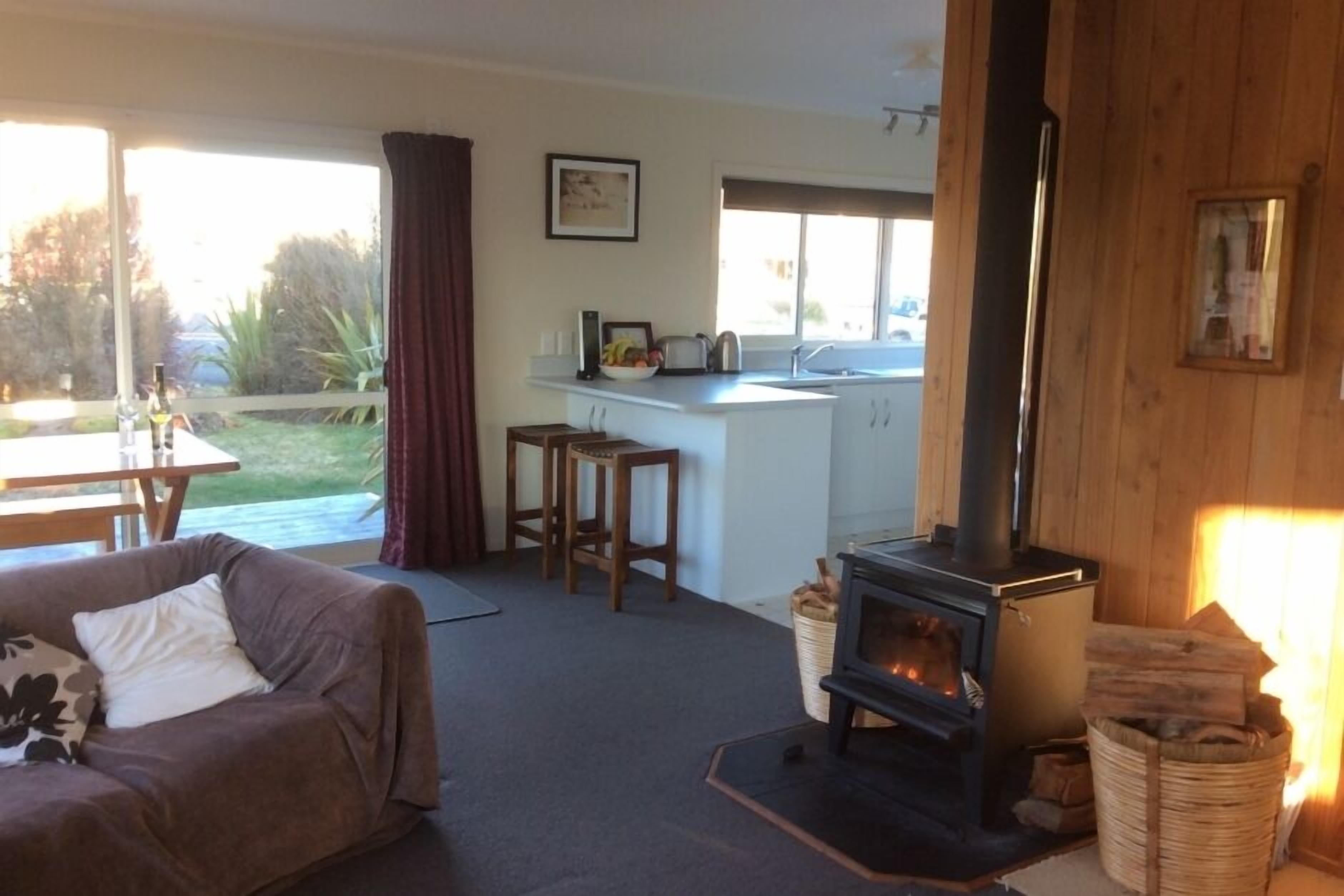 A cozy living room with a sofa, a fireplace, and a kitchen area with a window and a counter.