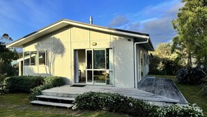Een modern huis met twee verdiepingen, een plat dak, grote glazen schuifdeuren en een klein voortuintje.