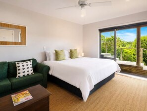 Une chambre à coucher avec un lit, un canapé vert, une table basse en bois et une grande fenêtre donnant sur un paysage verdoyant.