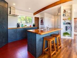 A modern kitchen with a central island, wooden stools, and a built-in bookshelf.