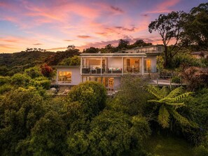 Une maison à deux étages dotée d’un balcon, entourée d’une végétation luxuriante.