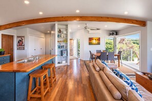 A modern kitchen with a wooden bar, a dining area with a view, and a living space with a sofa.