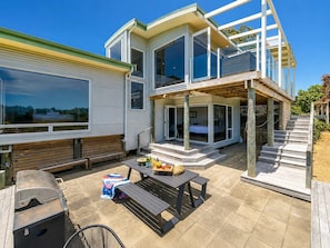 A modern two-story house with a patio area, a barbecue grill, and a dining table.