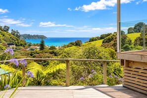 A wooden deck with a view of a coastal landscape, including a body of water and greenery.