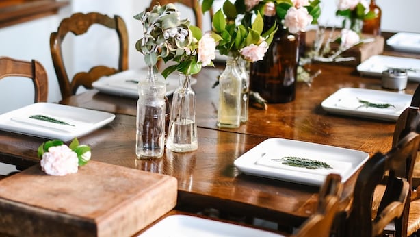A wooden dining table set with white plates, clear glass vases with flowers, and a wooden centerpiece. - Christmas 2026 Availability (Bundanoon)