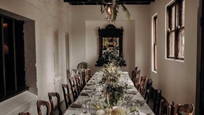 A long dining table set for a formal meal with chairs on both sides, a floral centerpiece, and a hanging light fixture above. - Christmas 2026 Availability (Bundanoon)