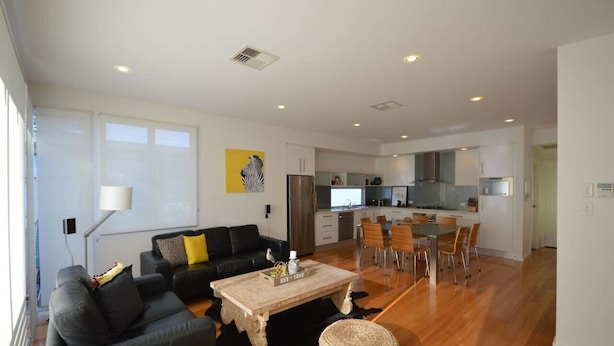 A modern living room with a sofa, coffee table, and dining area with chairs. - The Holdfast Townhouse Sussex St Glenelg (Glenelg)