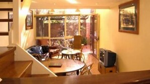 A cozy room with a wooden staircase, a dining area with a table and chairs, and a television on a wooden cabinet. - Stanley Cottage 2 bedroom (North Adelaide)
